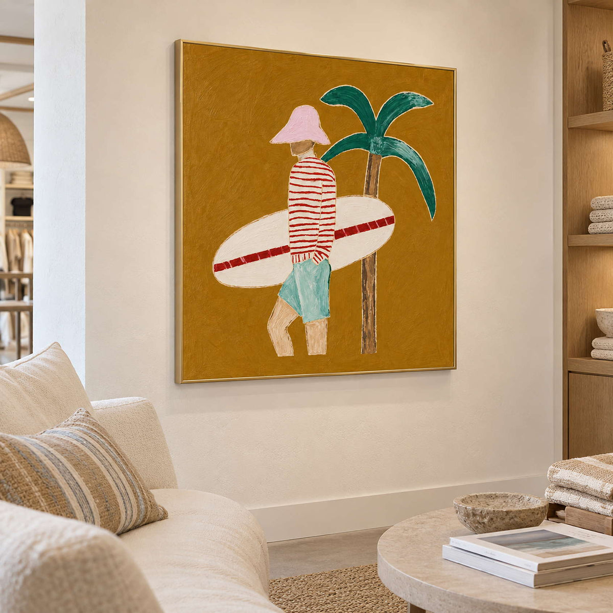 Pink-hatted surfer painting above a pale sofa near open shelving and a round coffee table.