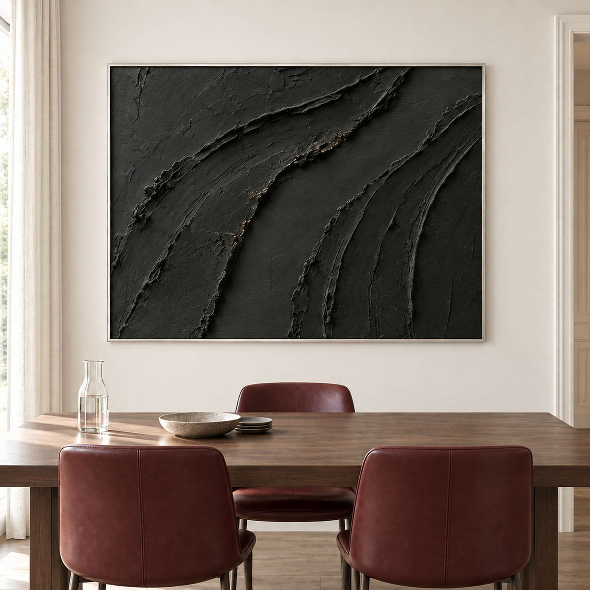 Sweeping raised black ridges with subtle gold accents in a silver frame, displayed above a dining table.