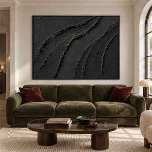 Sweeping raised black ridges with subtle gold accents in a black frame, displayed above a sofa in a living room.
