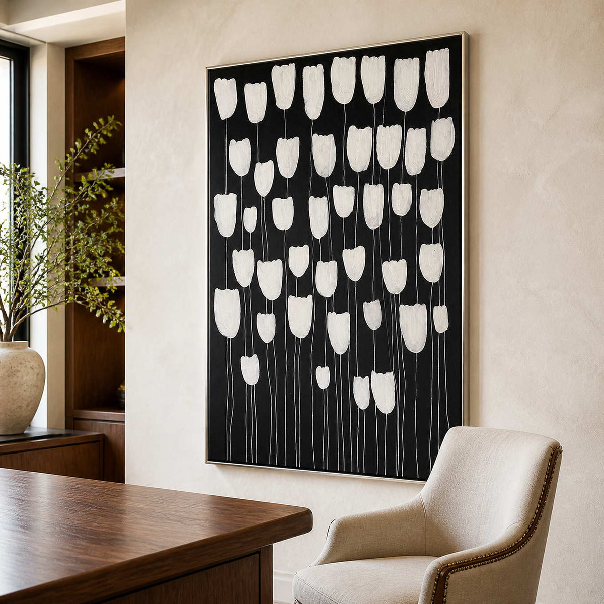 Silver framed white flower painting beside a wooden desk in a sunlit study.