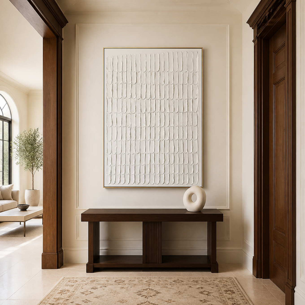 Gold framed cream abstract artwork above a dark wooden console in a bright hallway.