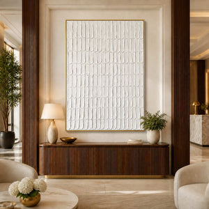 Gold framed cream abstract artwork above a fluted wooden cabinet in a hotel lobby.