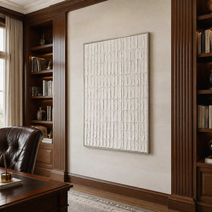 Silver framed cream textured artwork between bookshelves in a wood paneled study.