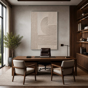 Silver framed beige relief artwork behind a wood desk in a booklined office.
