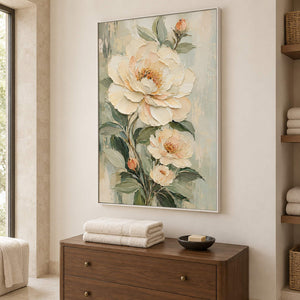 Cream flowers and soft green leaves on a muted background in a white frame, displayed in a bathroom dry area.