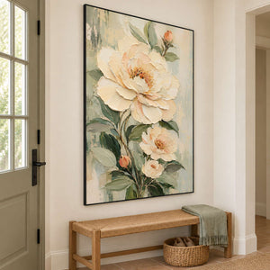 Cream flowers and soft green leaves on a muted background in a black frame, displayed above an entryway console.