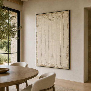 Black framed cream textured artwork beside a round wooden dining table and sunlit window.