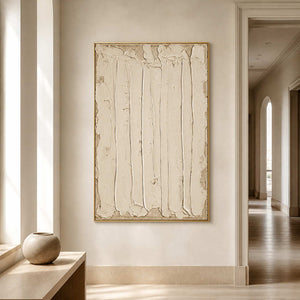 Gold framed vertical cream abstract artwork beside a console in a bright hallway.