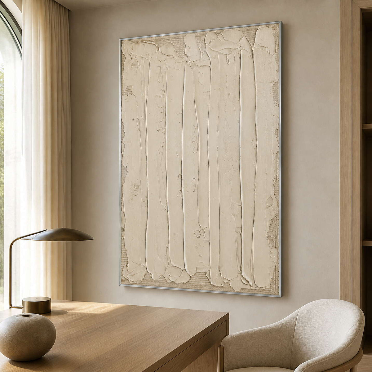Silver framed cream textured artwork beside a wooden desk in a softly lit study.