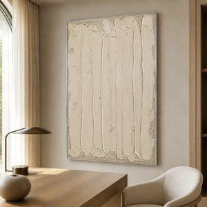 Silver framed cream textured artwork beside a wooden desk in a softly lit study.