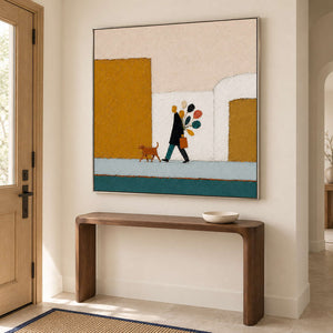 A figure walking a dog past mustard buildings with a colorful bouquet in a silver frame, displayed above an entryway console.