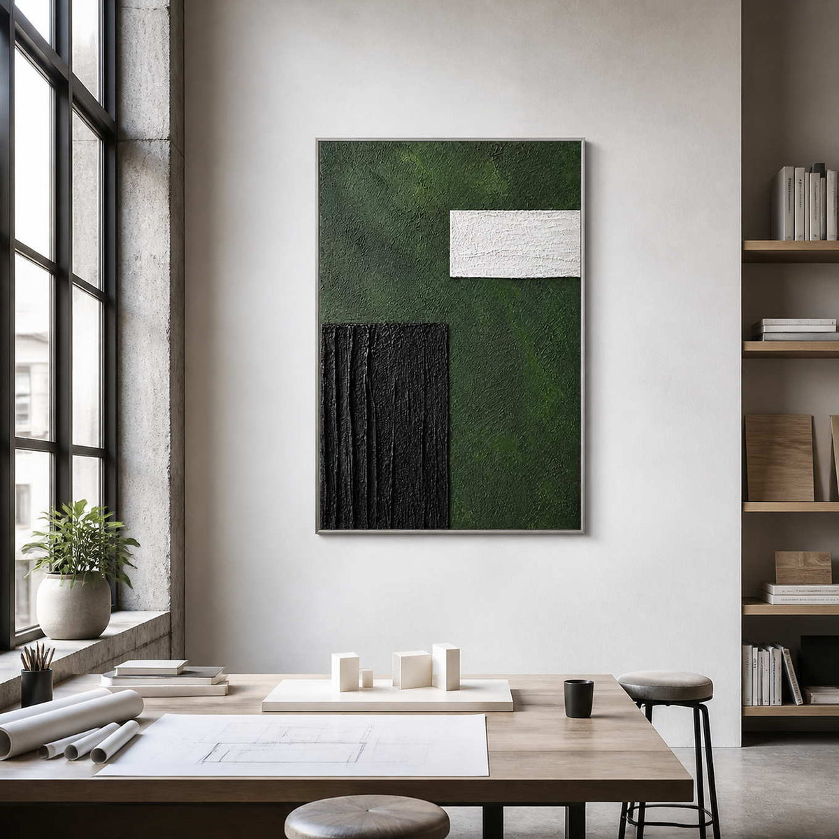 Silver framed textured geometric painting above architectural models and drawings in a studio.