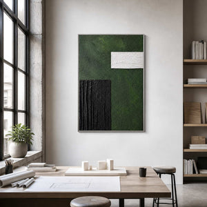 Silver framed textured geometric painting above architectural models and drawings in a studio.