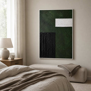 White framed green abstract artwork displayed beside a bed and upholstered bedroom bench.