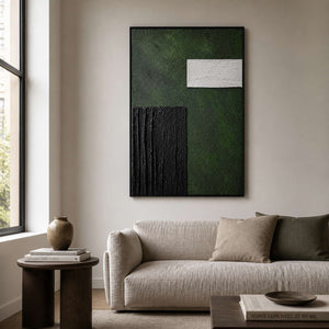Black framed green abstract painting above a pale sofa in a modern apartment.