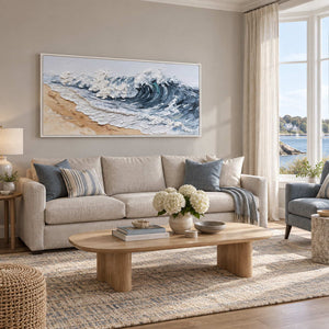 A Letter from the Waves in a white frame above a cream sofa beside a window overlooking water.