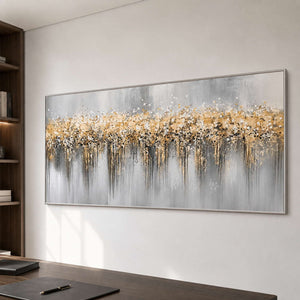 Silver framed gold and gray abstract painting beside a desk and dark wood bookshelves.