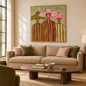 A Meeting in Style in a gold frame above a tan sofa with pink and green cushions and an oval wood table.