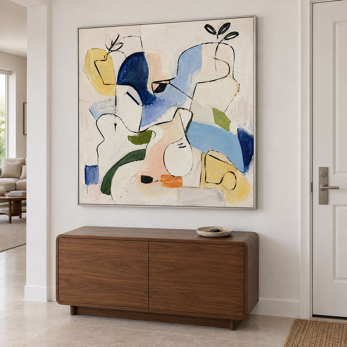 Loose black outlines and blue, yellow and green abstract shapes in a silver frame, displayed above an entryway console.