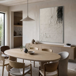 Silver framed pale abstract artwork above a sideboard beside a light oval dining table.