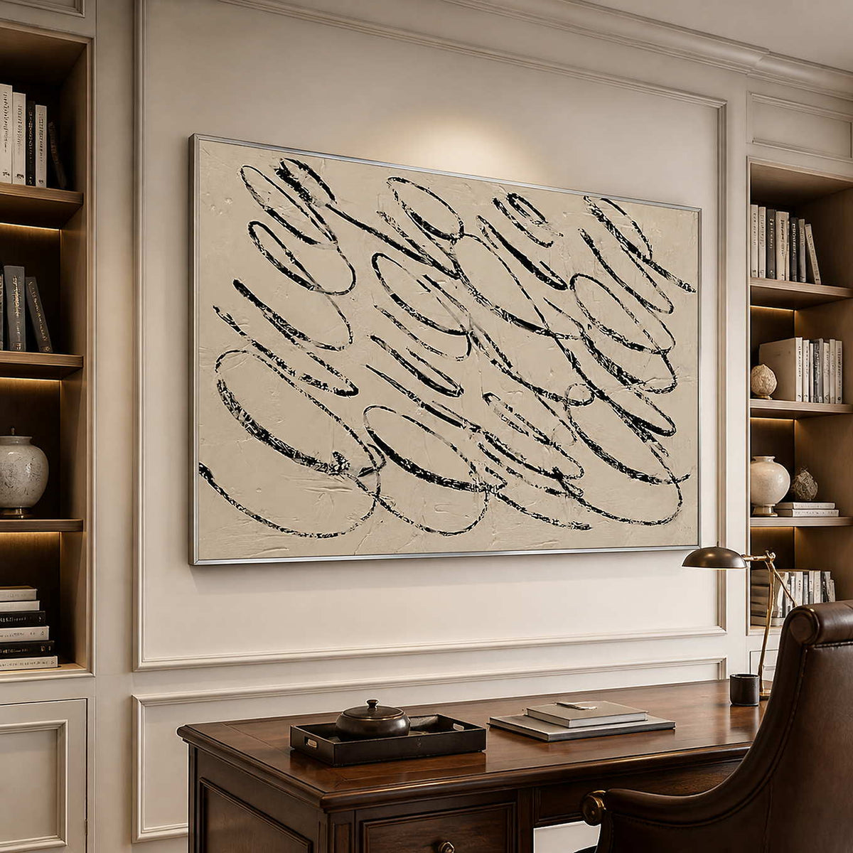 Silver framed abstract loops above a wooden desk between illuminated bookshelves.