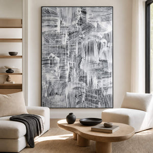 Tall monochrome abstract painting behind cream lounge chairs and a round coffee table.