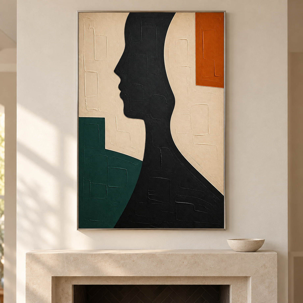 Hand-painted black profile canvas with ivory, green, and orange forms, displayed beside or above a fireplace in a silver frame.