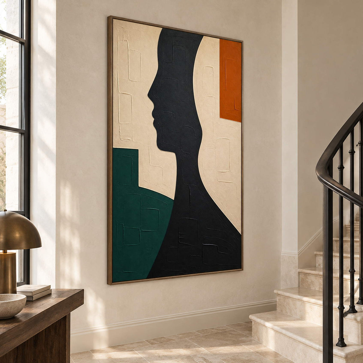 Hand-painted black profile canvas with ivory, green, and orange forms, displayed beside a staircase in a brown wood frame.