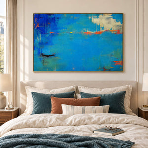 Blue and turquoise abstract painting with narrow orange streaks in a gold frame in a bedroom.