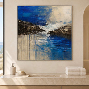 Square cobalt sea, dark rock, and ivory surf textured painting, displayed in a bathroom dry area in a silver frame.