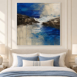 Square cobalt sea, dark rock, and ivory surf textured painting, displayed in a bedroom in a white frame.