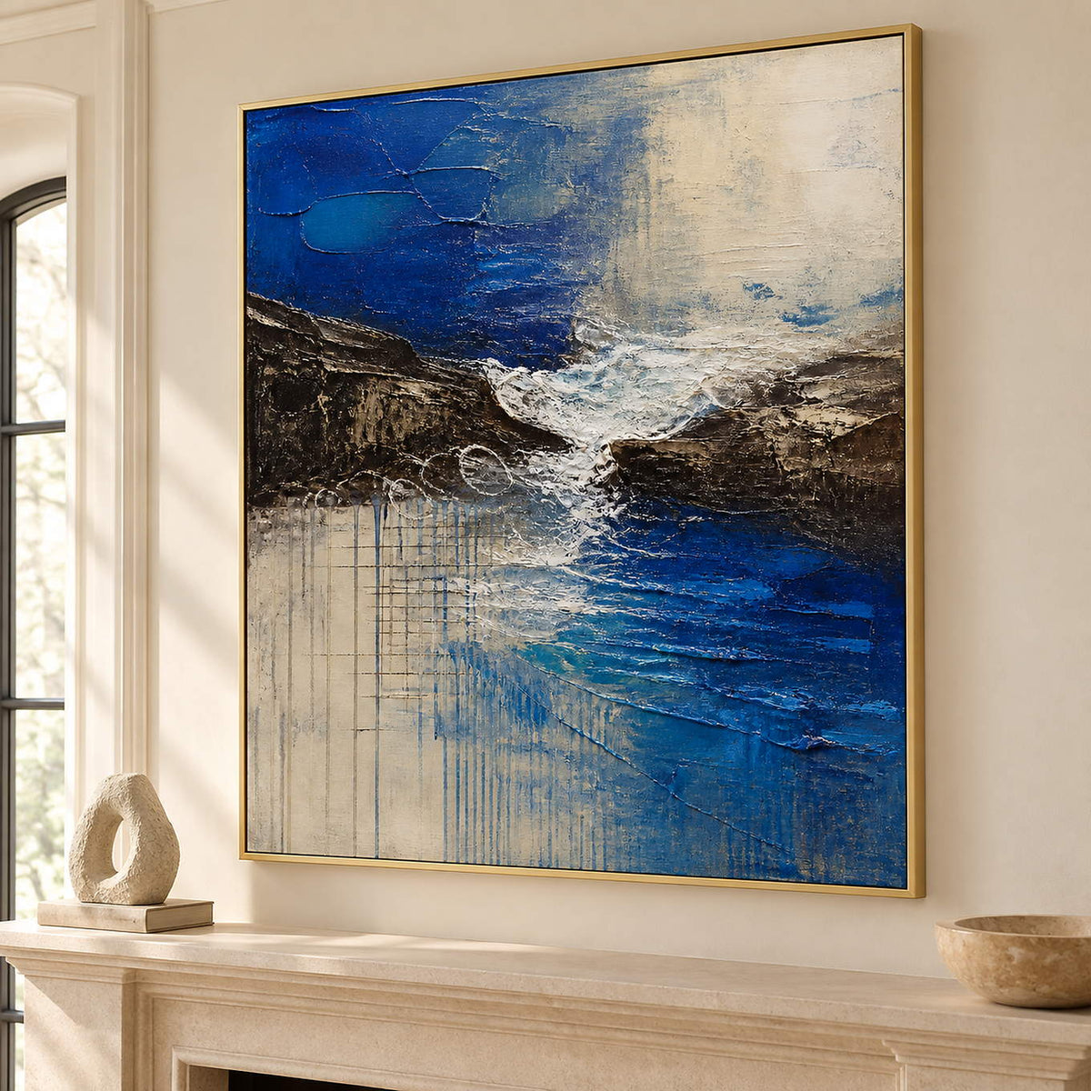 Square cobalt sea, dark rock, and ivory surf textured painting, displayed beside or above a fireplace in a gold frame.