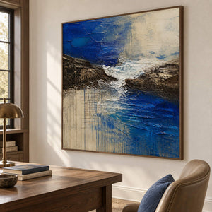Square cobalt sea, dark rock, and ivory surf textured painting, displayed in a study in a brown wood frame.