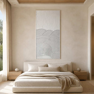 White framed textured artwork above a neutral bed with soft layered linens.