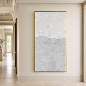 Gold framed white abstract artwork on a pale wall in a sunlit hallway.