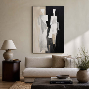 Black framed painting of two pale figures above a sofa in a neutral living room.