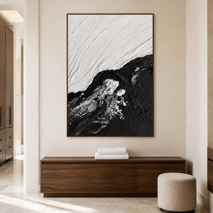 Wood framed monochrome artwork above a cabinet with folded towels beside an ottoman.