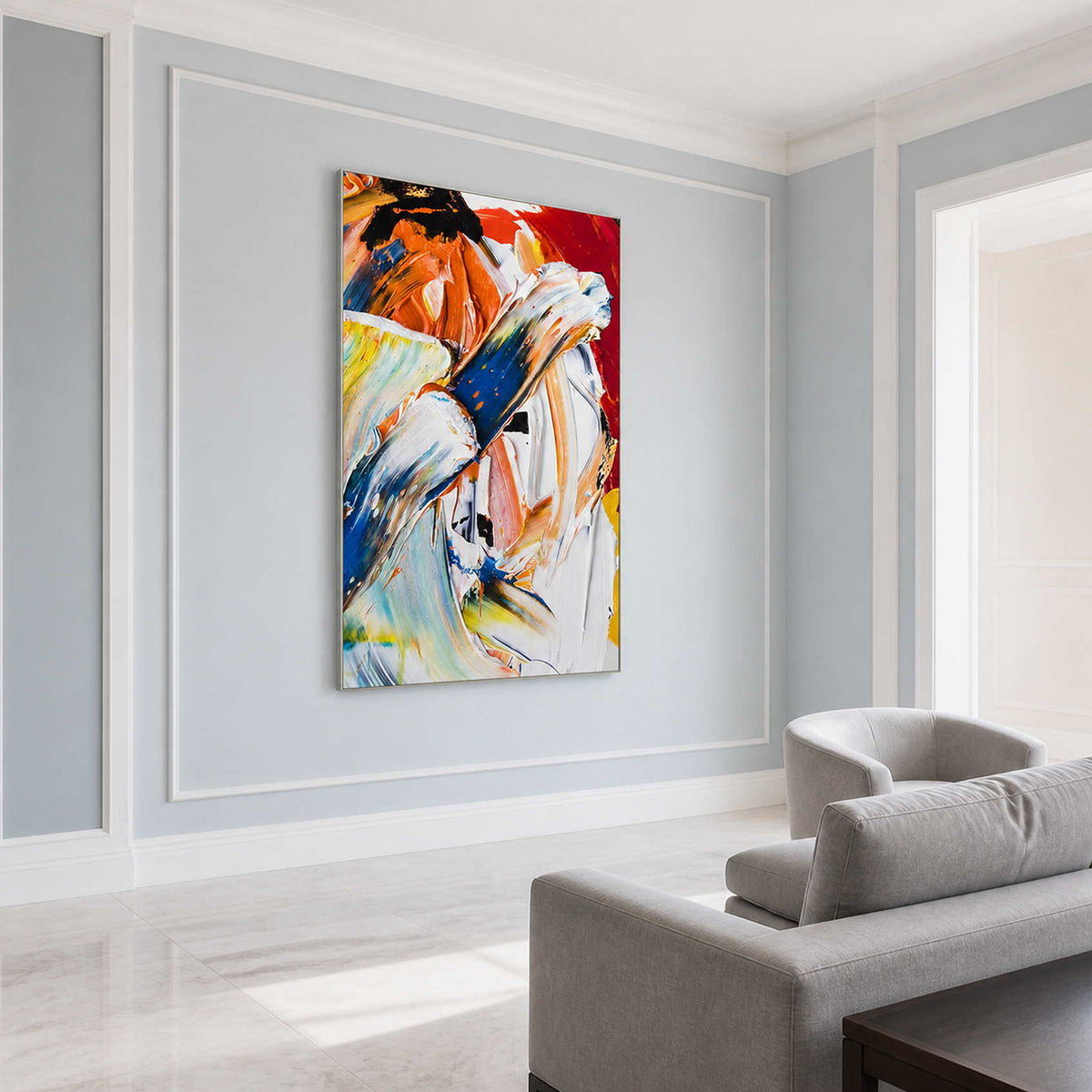 Silver-framed blue and white abstract painting on a pale blue-gray wall beside a light gray sofa.