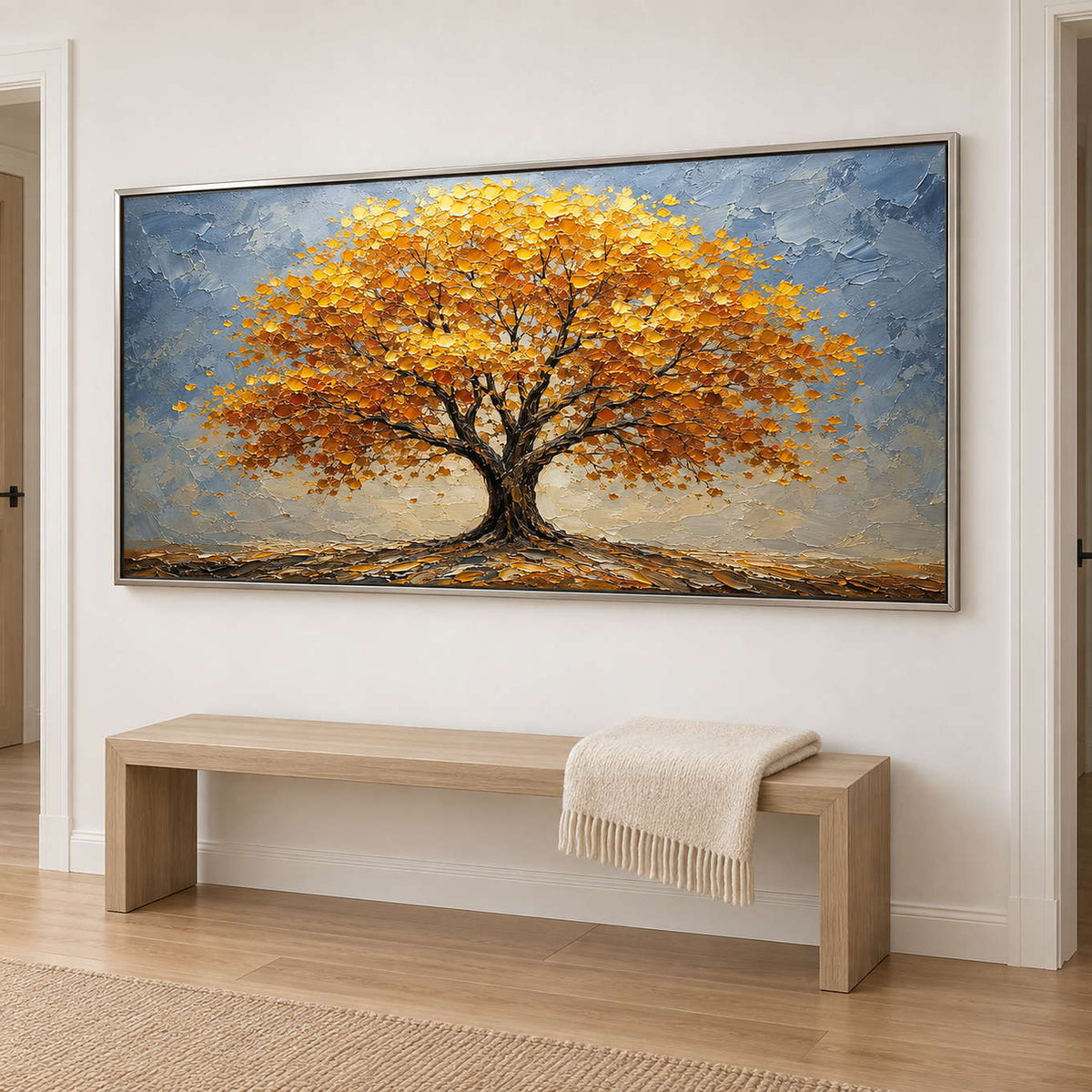 A broad golden autumn tree beneath a gray-blue sky in a silver frame, displayed in a hallway.
