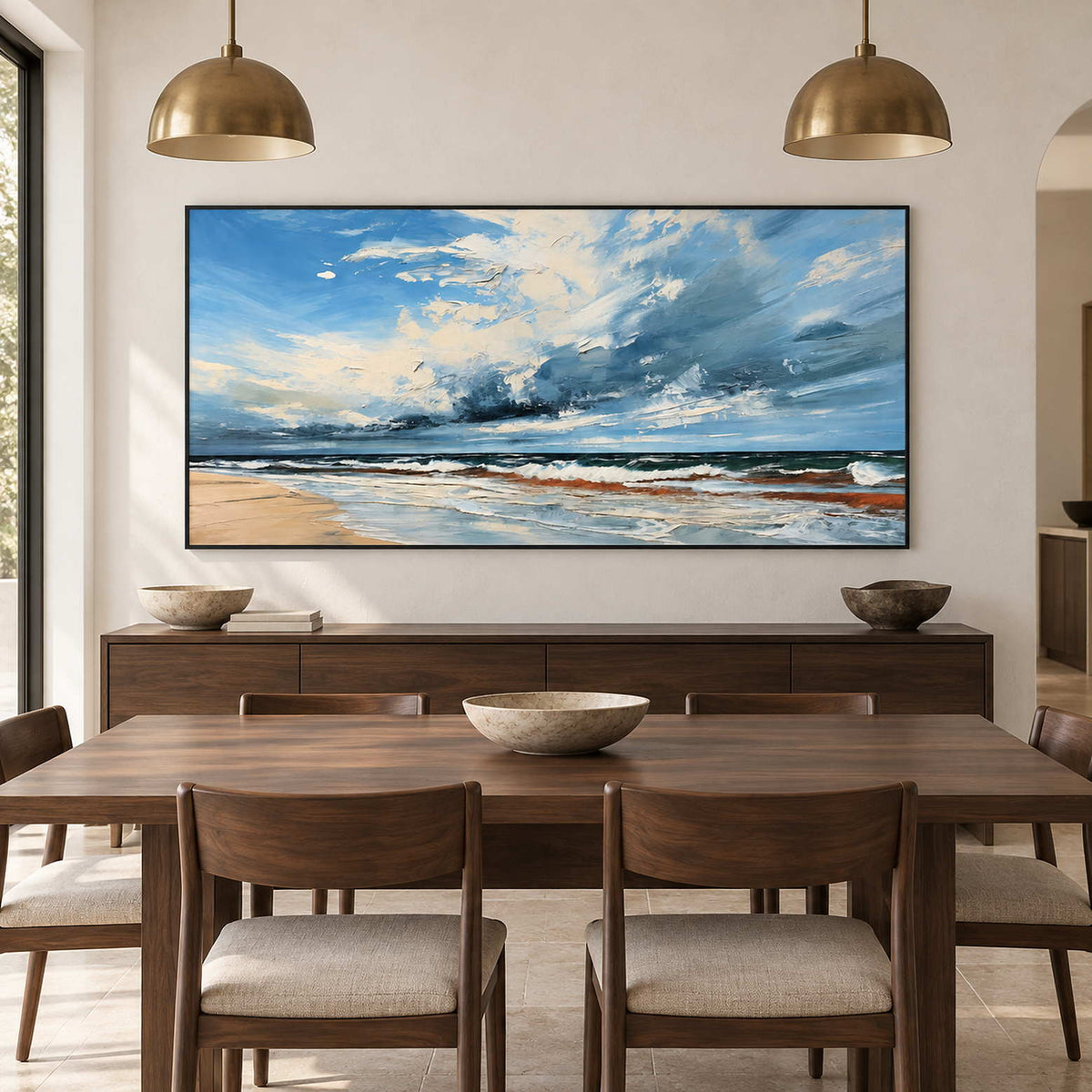 Cloud-filled coast painting above a brown sideboard under two gold-toned pendant lamps.