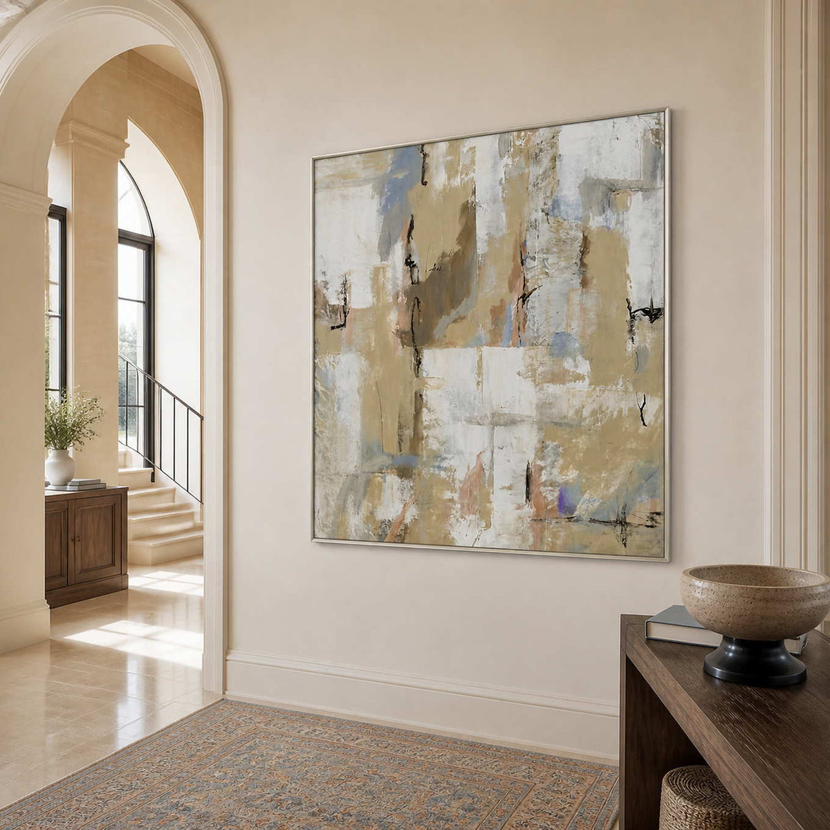 Silver-framed cream and blue-gray artwork beside an arched entryway leading to a bright staircase.