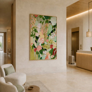 Gold framed botanical artwork beside a hotel reception desk and elevator with suitcase.