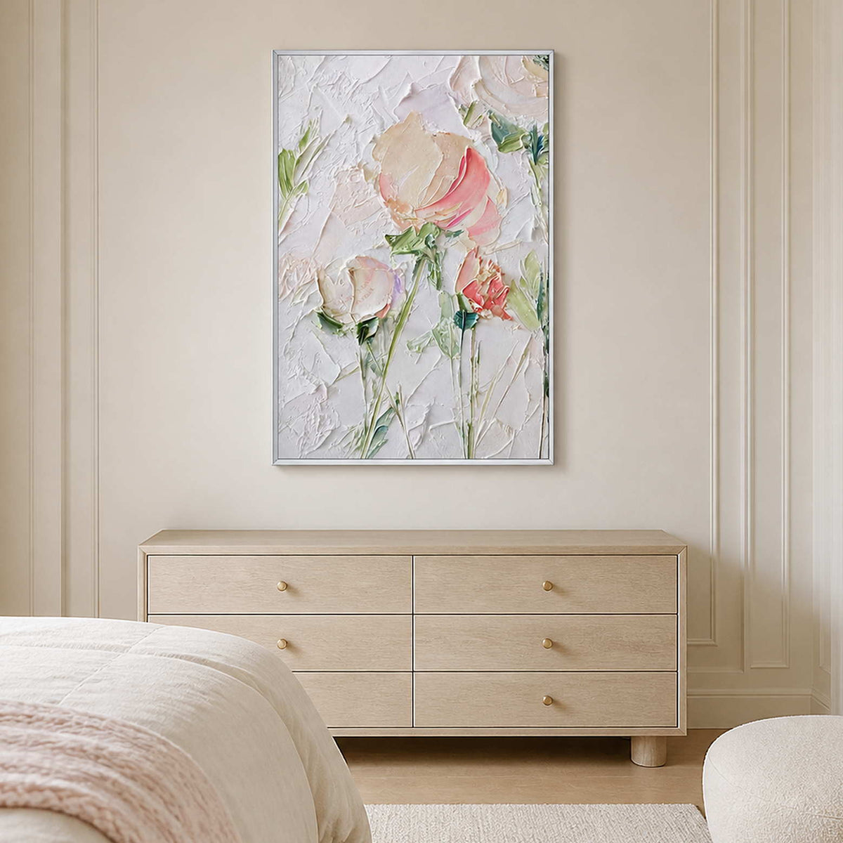 White framed pink floral painting above a pale dresser beside a cream bed.