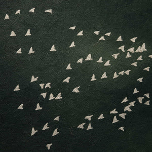 Close-up of ivory bird forms against layered forest-green texture.