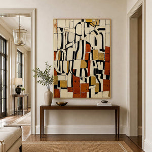 Gold framed earthy geometric painting above a slim console and leafy vase in an entryway.