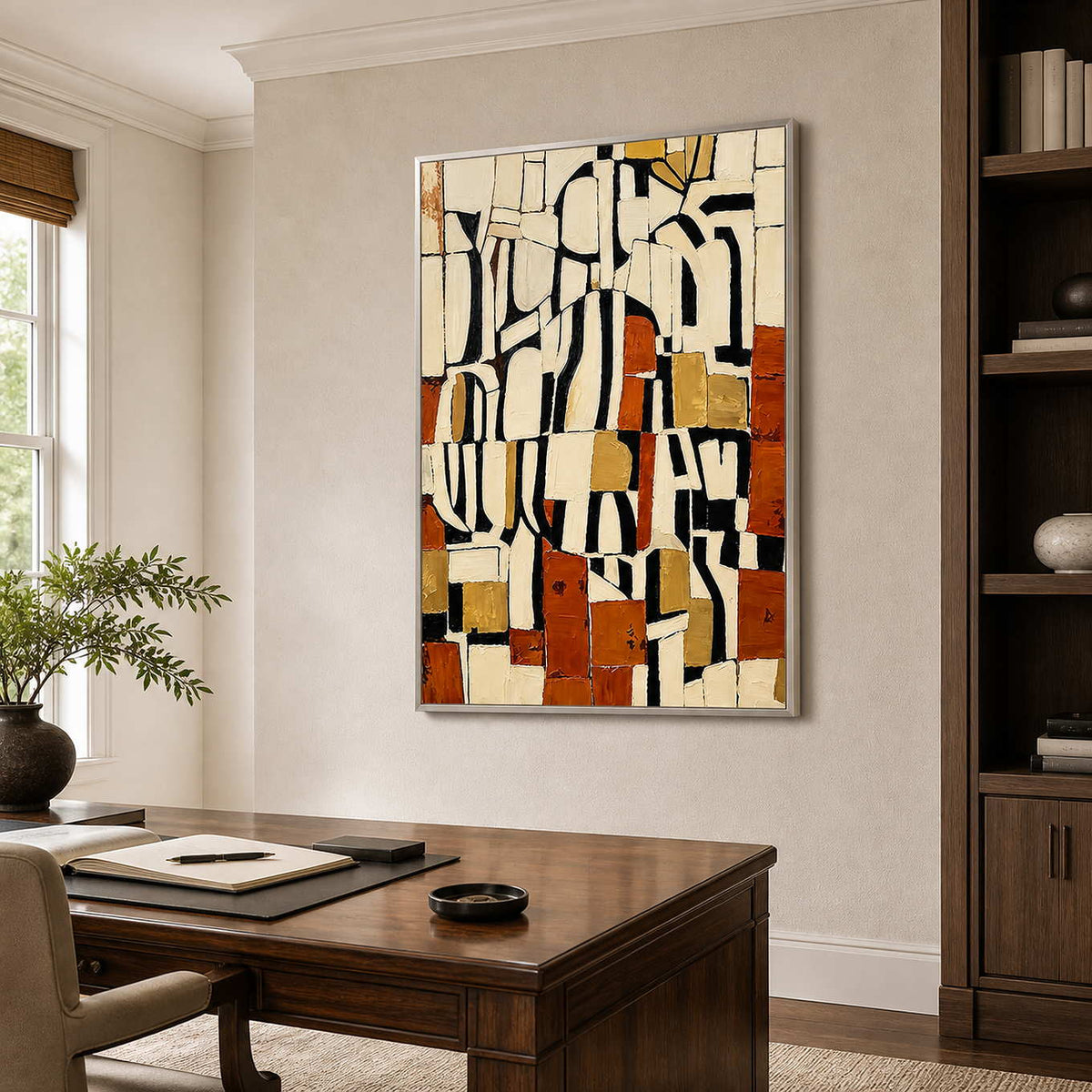 Silver framed cream and rust geometric artwork beside a desk and bookshelves in a study.
