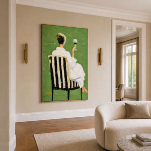 Gold framed painting of a woman raising wine beside a cream sofa in warm light.
