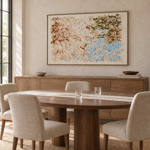 A Visit from Spring in a wood frame above a long sideboard behind a round dining table with cream chairs.