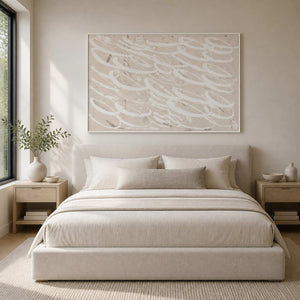White framed beige abstract painting above a cream bed in soft daylight.