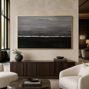 Gold framed gray horizon painting above a cabinet near hotel lobby lounge chairs.